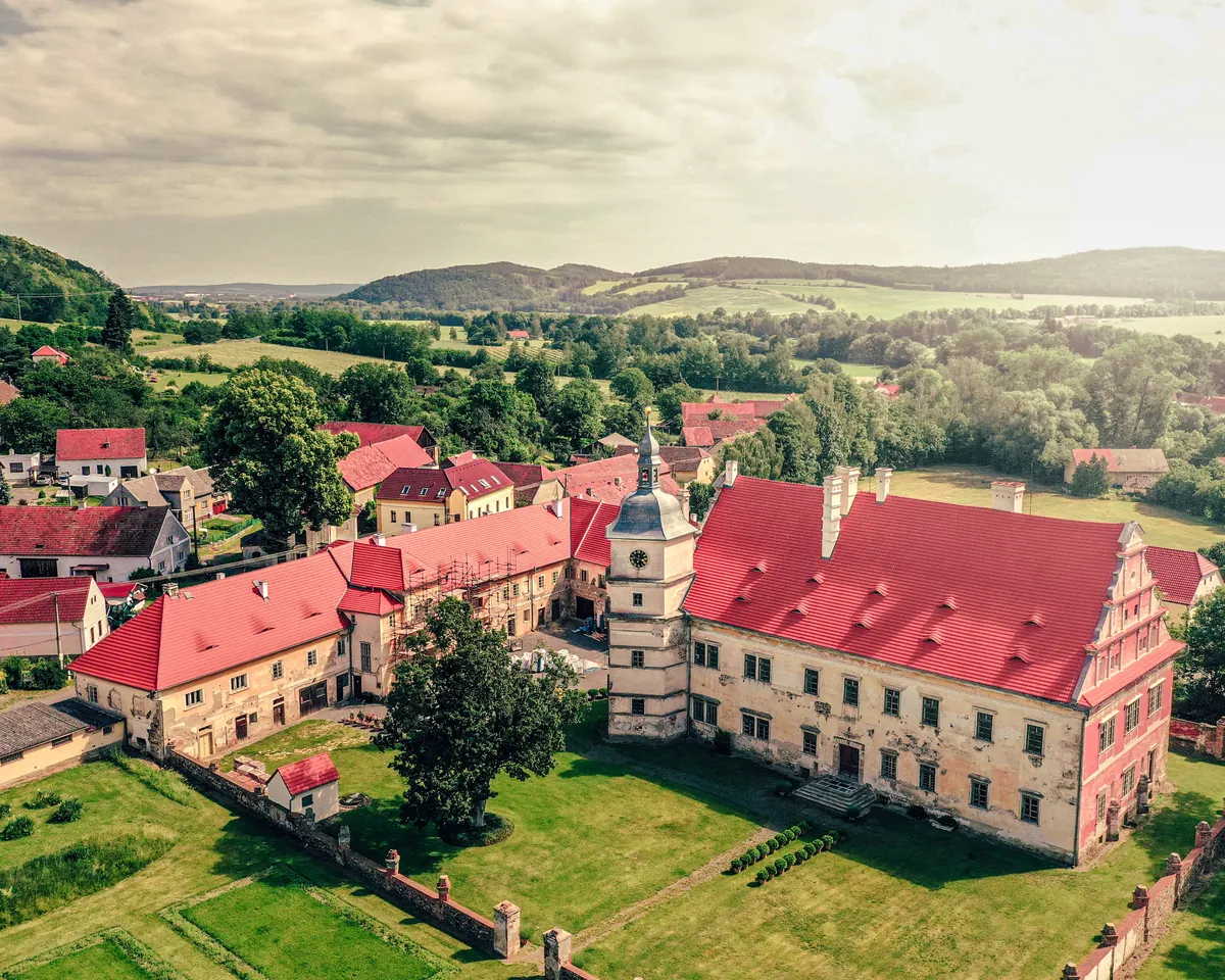 Letecký pohled na zámecký areál s červenými střechami a okolní krajinu